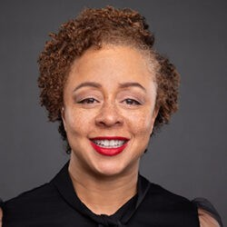 Headshot photo of Denine Das who is facing the viewer and smiling. She is wearing red lipstick and a black short sleeve blouse.